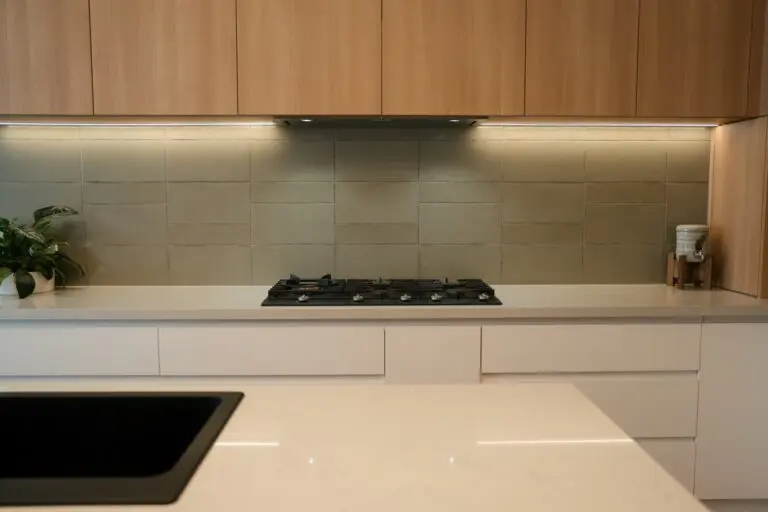 Light oak cabinetry with a green glass splashback and gas cooktop