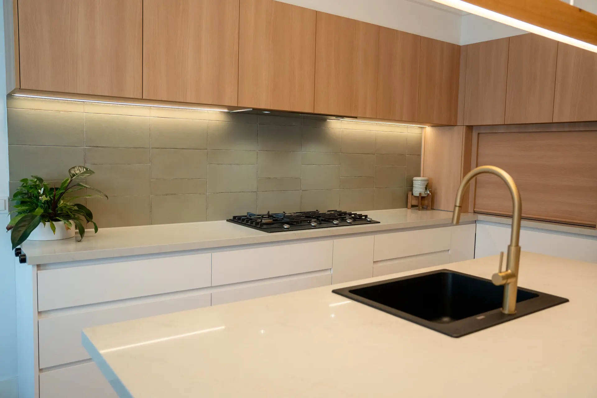 Warm oak cabinetry with a black undermount sink and brass tapware