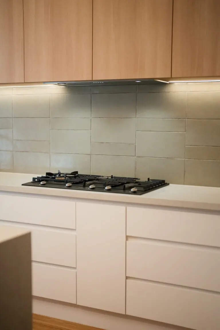 Light oak cabinetry with a green splashback above a gas cooktop
