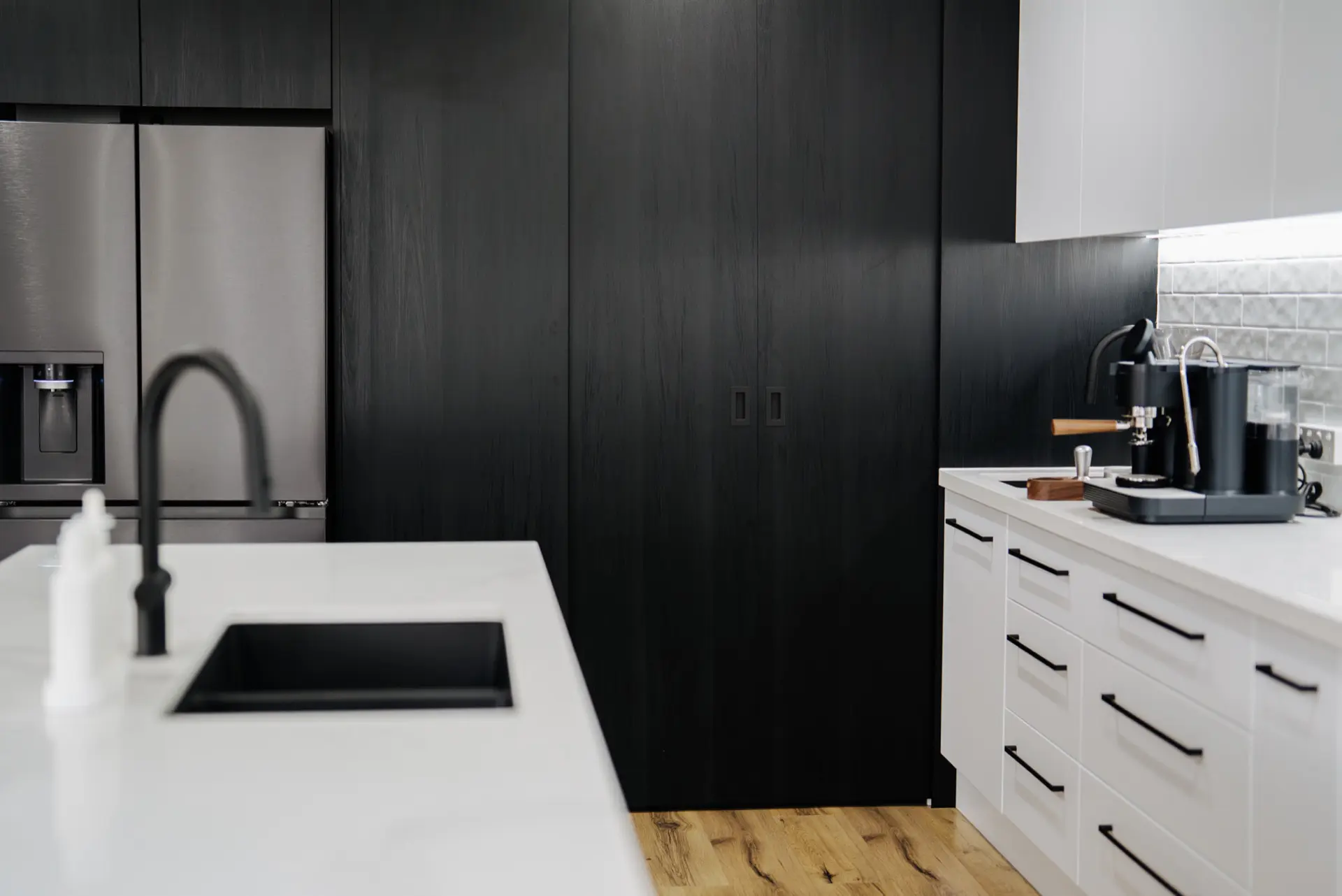 Matte black tall cabinetry with an integrated fridge beside a white stone island