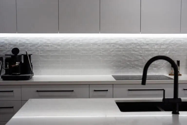 A white stone benchtop with black tapware and a textured splashback