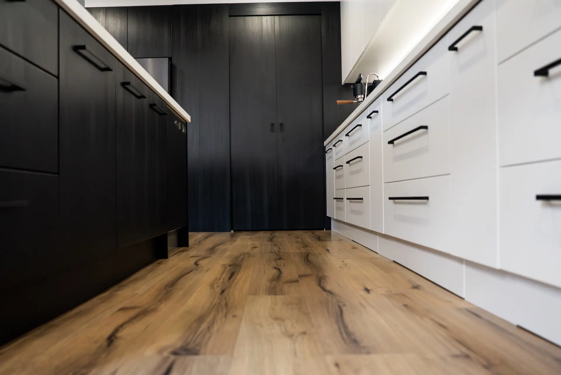 A matte black kitchen with white cabinetry and timber flooring