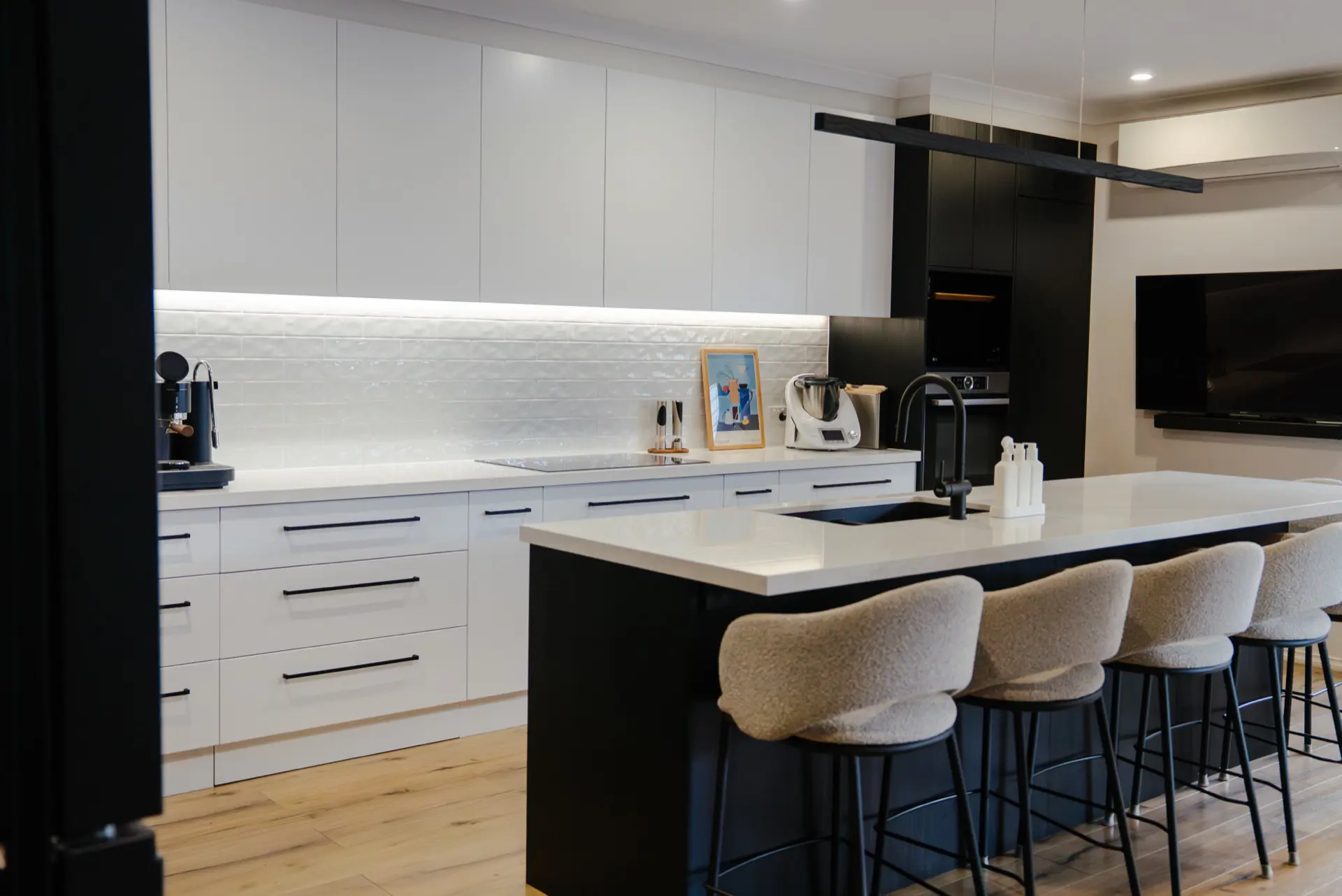 A matte black and white kitchen with a long stone island and upholstered stools