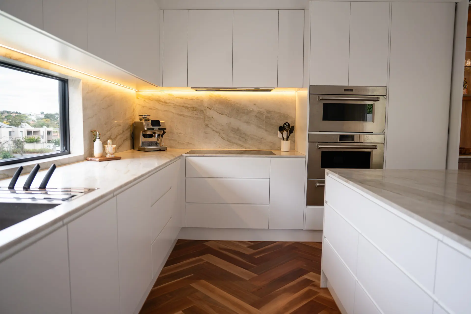 A modern white kitchen with marble benchtops over herringbone parquet flooring