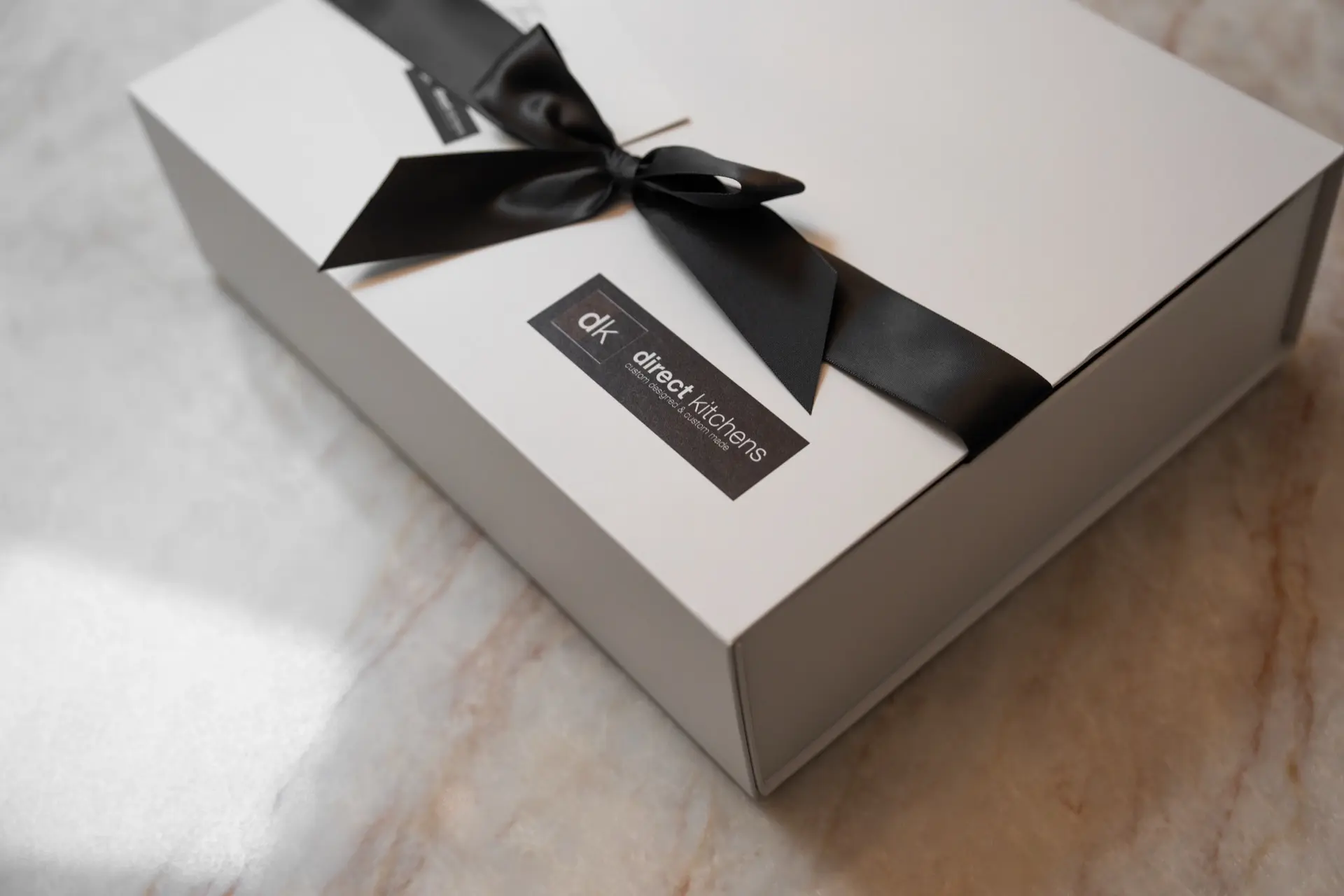 A Direct Kitchens gift box tied with a black ribbon on a marble benchtop